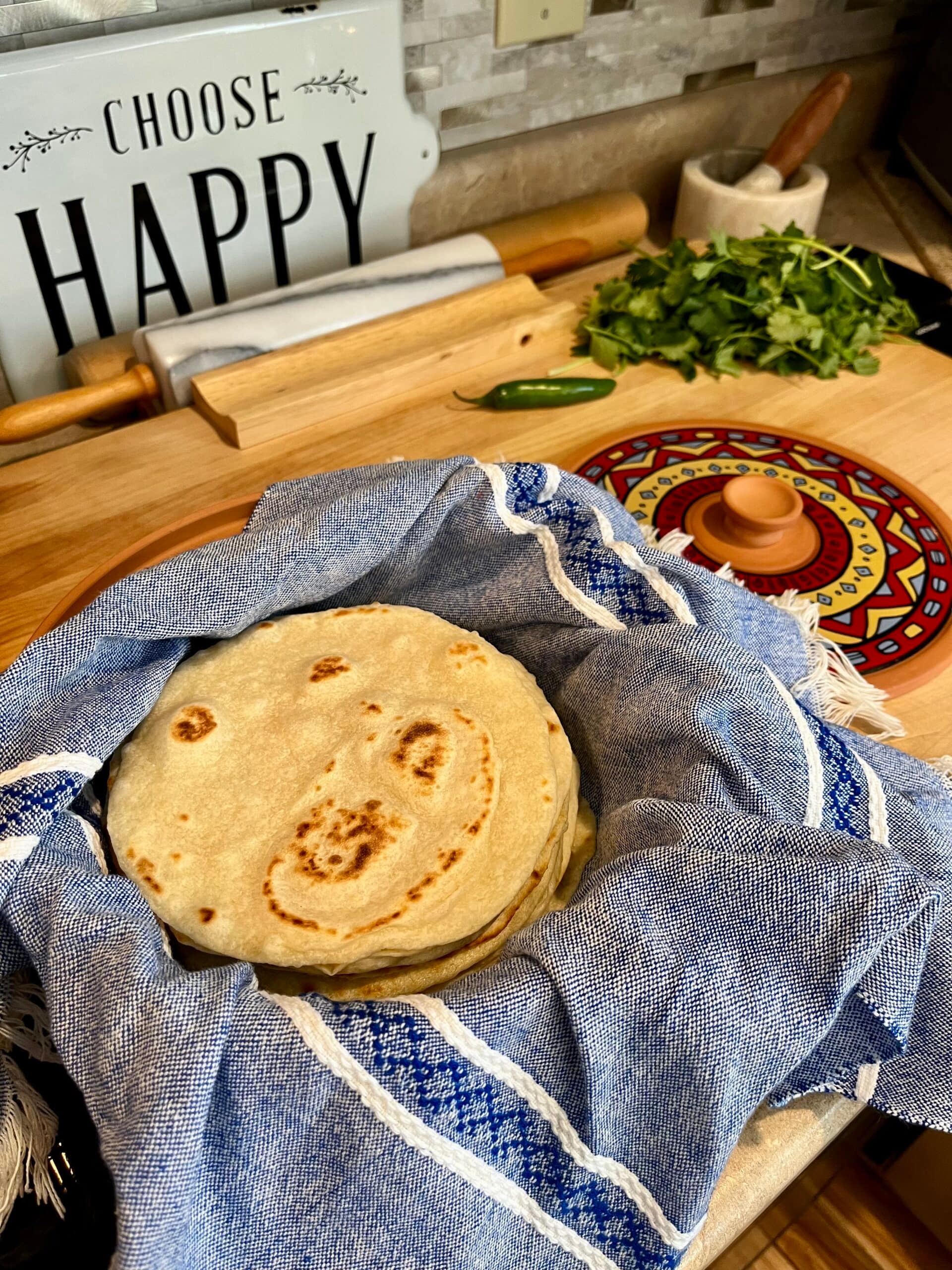 tortillas made with fresh milled flour in basket next to choose happy sign, rolling pin.